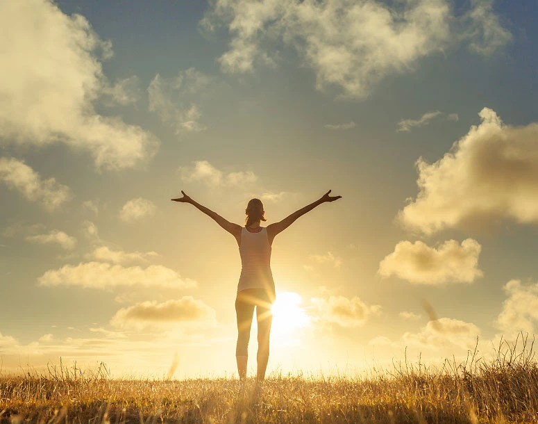 Woman standing in a golden field with arms wide open, embracing the sun